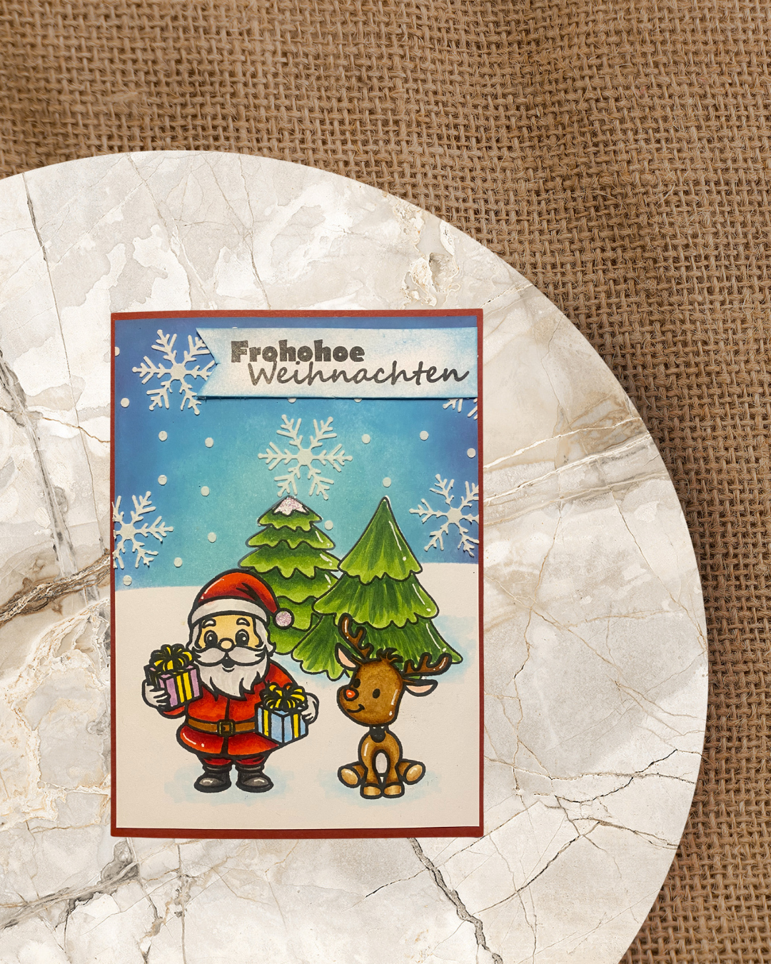 Karte mit dem Nikolaus und Rentier. Im Hintergrund Tannenbäume und Schneefall