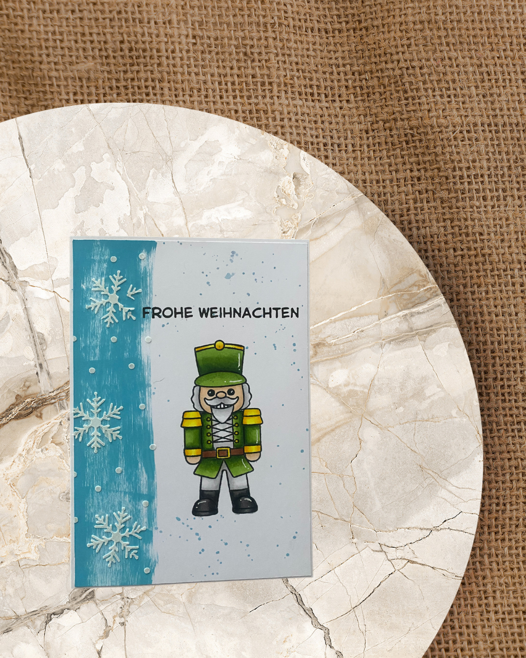 Weihnachtskarte mit einem Nussknacker, im Hintergrund Eiskristalle und Frohe Weihnachten