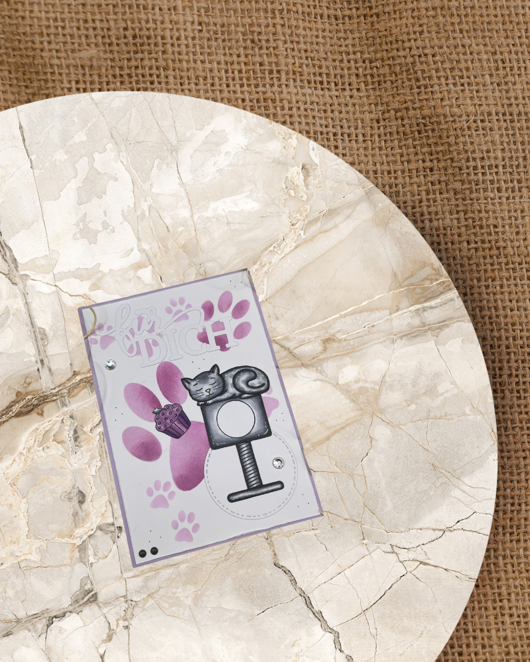 Schafende Katze auf einem Kratzbaum. Im Hintergrund verschieden große Tatzen in lila