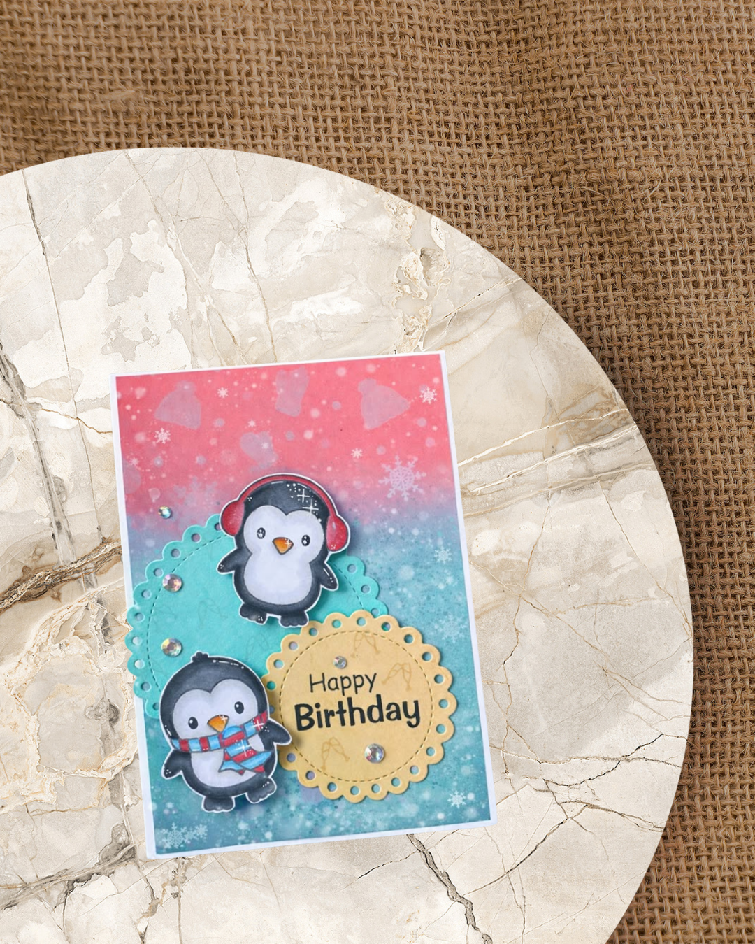 Rosa/blaue Karte mit Mütze, Handschuhen und Eiskristallen mit 2 Pinguine und dem Spruch Happy Birthday