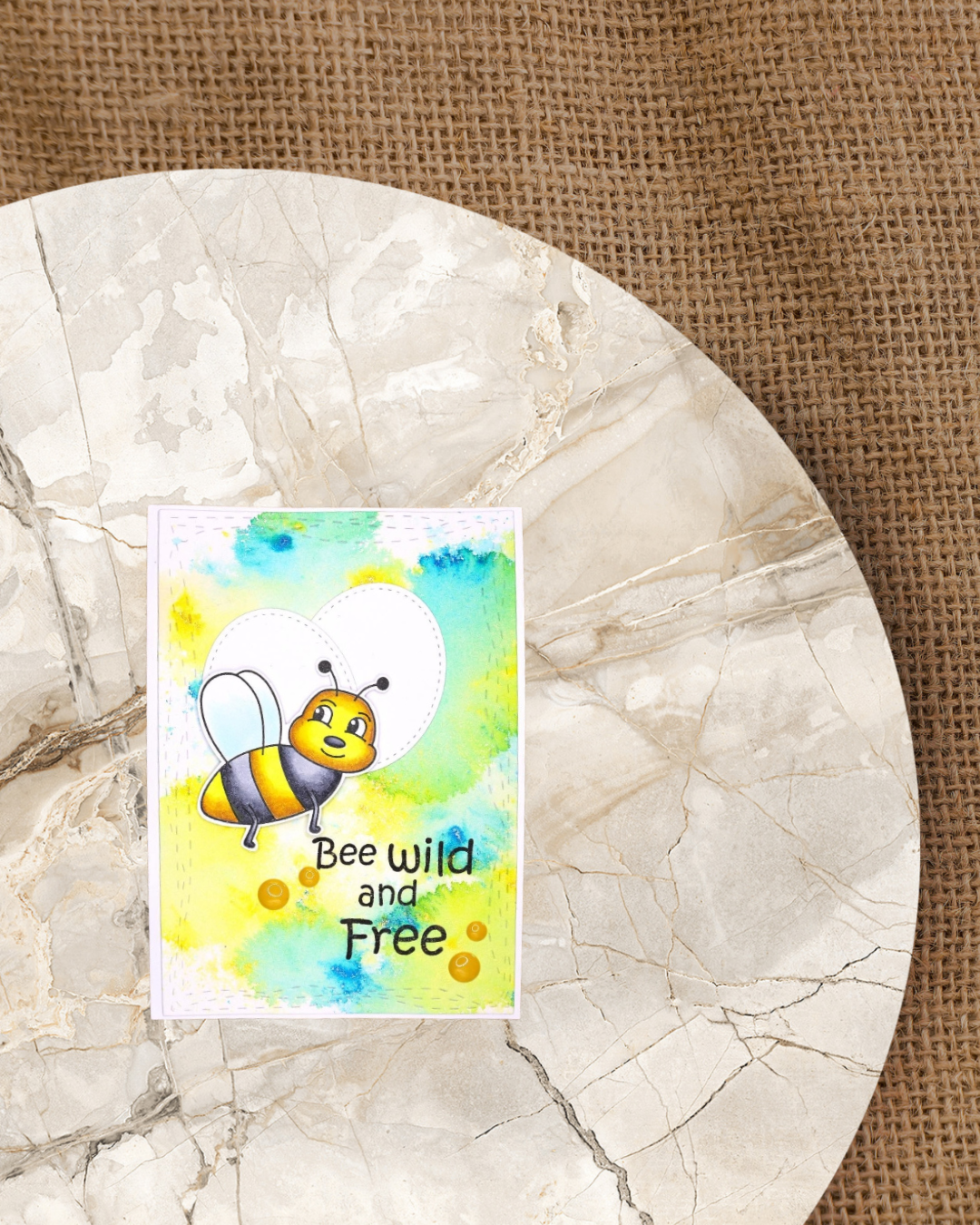 Fliegende Biene auf einer Karte mit Wasserfarbenhintergrund in Gelb und Blau. Spruch Bee Wild and Free