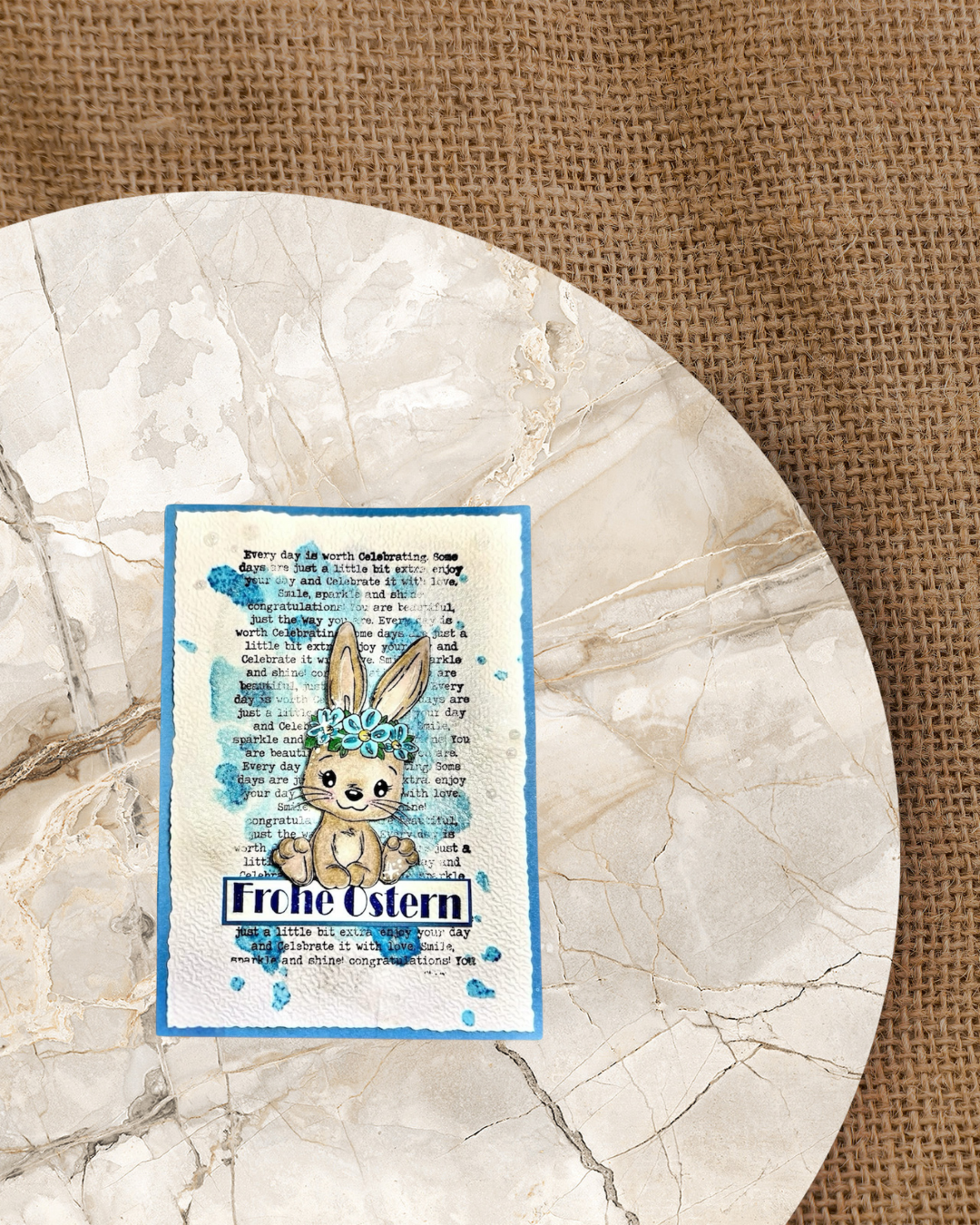 Hase mit Blumenkranz ist auf einem Spruchband mit Frohe Ostern im Hintergrund eine schwarze Schrift und blaue flecken