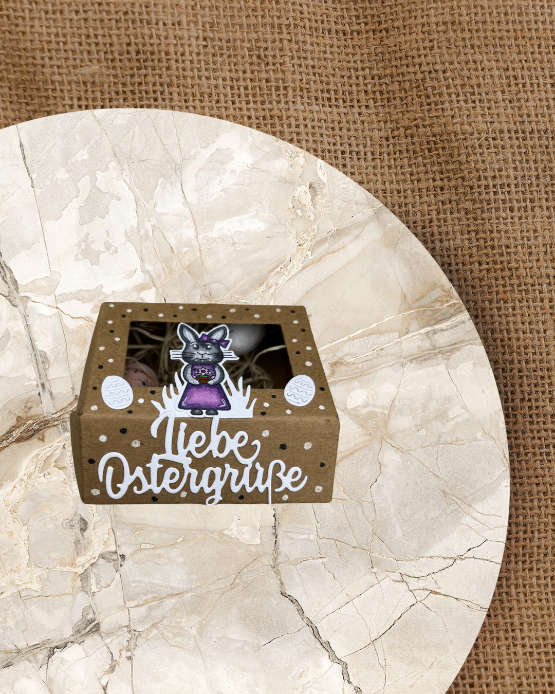 Kraftfarbene Bos mit schwarzen und weißen Punkten und 2 weißen Eiern. In der Mitte ein Hasenmädchen mit Blumentopf in den Pfoten und dem Spruch liebe Ostergrüße