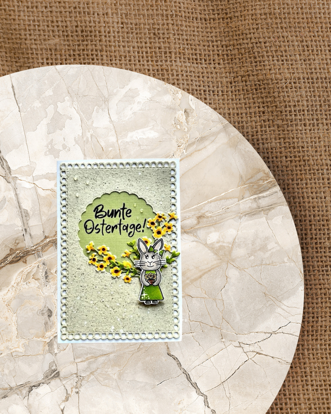 Karte zu Ostern mit einem Hasenmädchen mit Blumen in den Pfoten. Gelbe Blumen im Hintergrund und der Spruch Bunte Ostertage