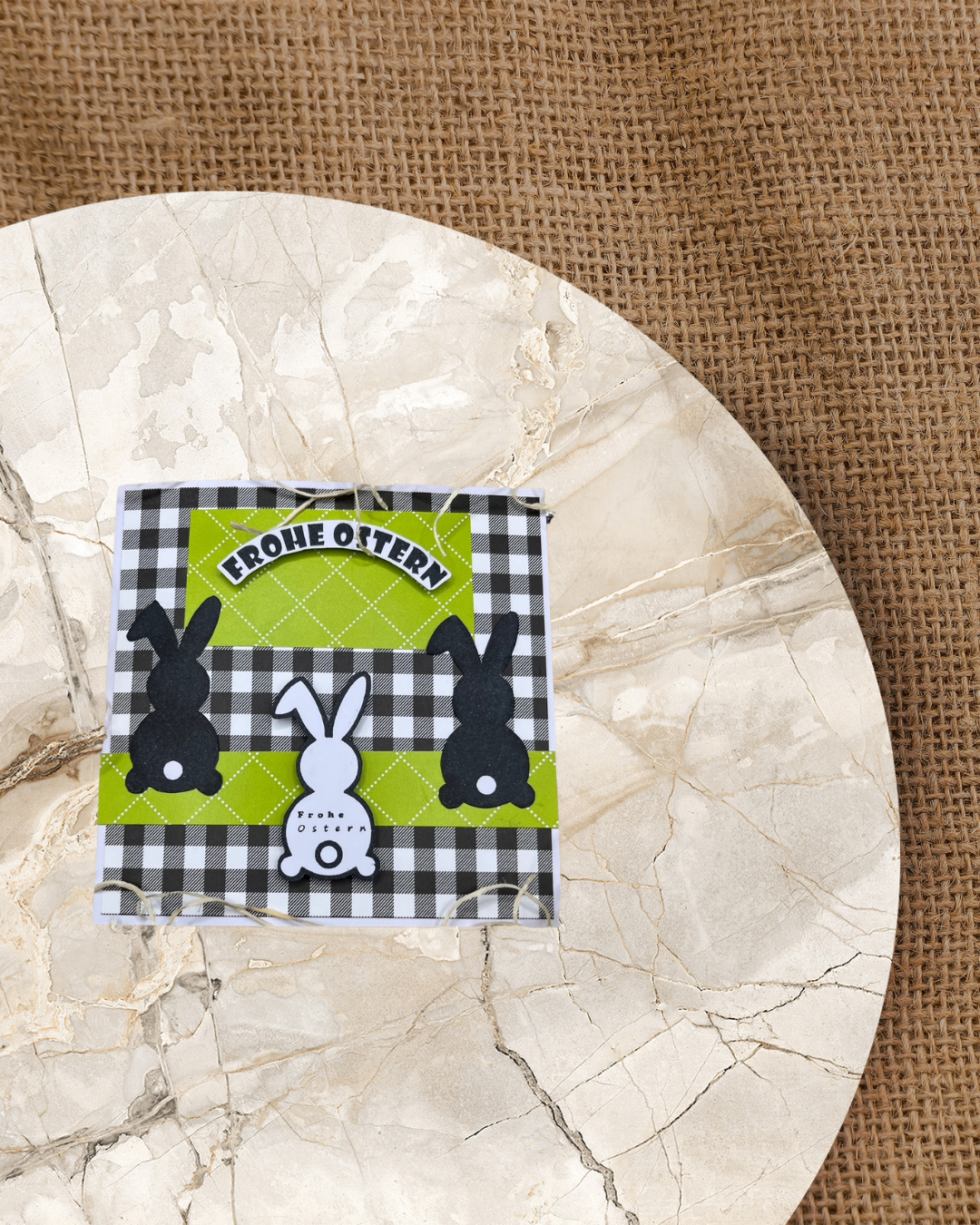 Karte mit 2 Schwarzen Hasen und einem Weißen Hase mit dem Spruch Frohe Ostern. Als Hintergrund einen grünen Mittelstreifen und kariertes Papier in schwarz/weiß