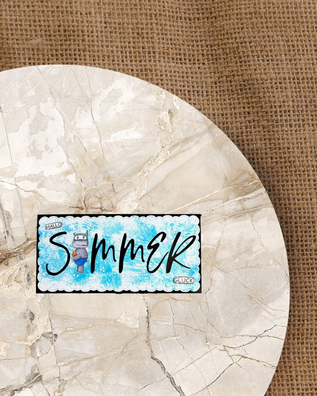 Din Lang Karte mit großen schwarzen Schriftzug Sommer. Das O wird durch ein Nilpferd in Badehose mit Taucherbrille und Cocktail in der Hand ersetzt. Links oben klein Hallo und rechts unten Glück. Hintergrundfarbe blau