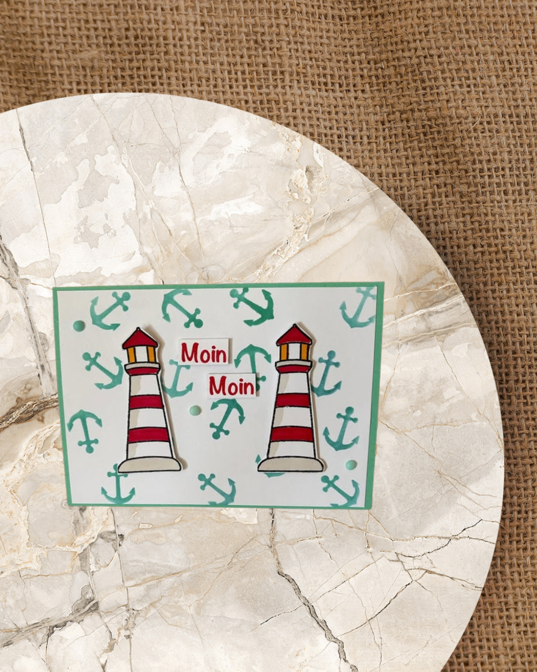Karte mit 2 Leuchttürme mit dem Spruch Moin Moin. Im Hintergrund viele Anker in Türkis