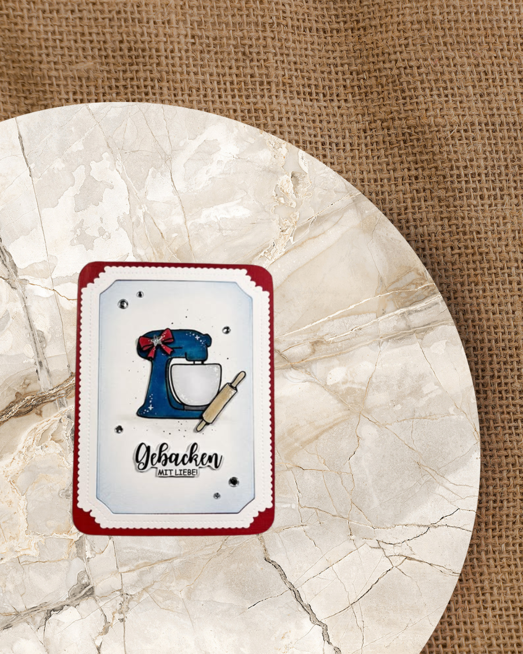 ATC mit einer blauen Rührschüssel und einem Nudelholz. Verziert noch mit einer Schleife und Glitzersteinen. Als Spruch Gebacken mit Liebe