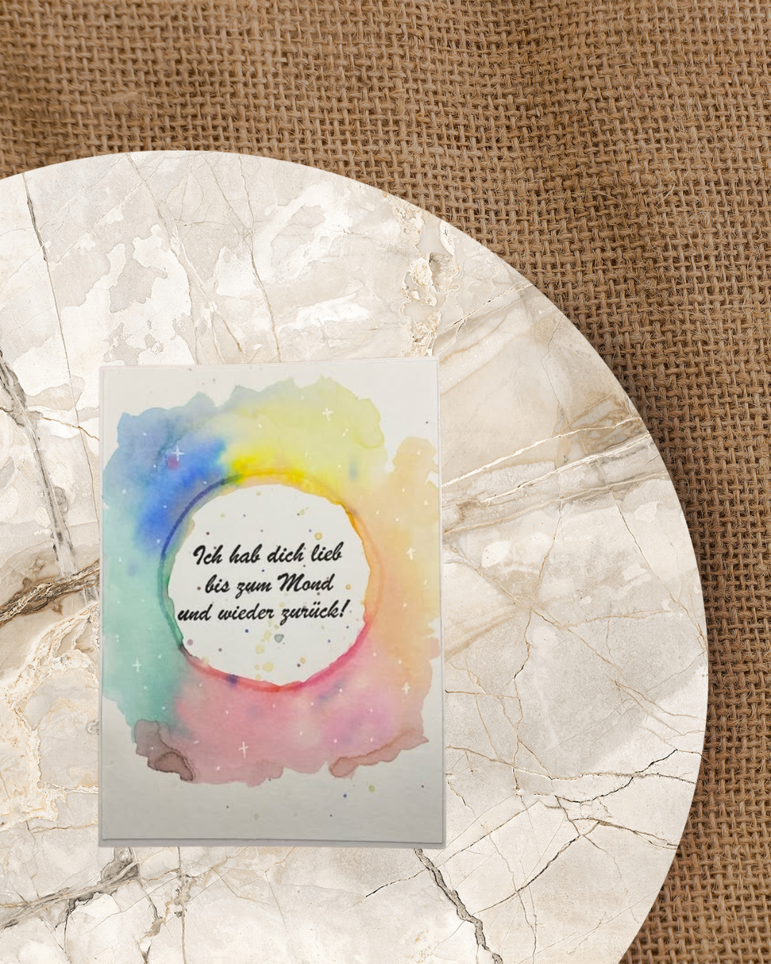 Karte mit einem Regenbogenfarbenen auslaufenden Kreis. In der Mitte der Spruch Ich hab dich lieb bis zum Mond und wieder zurück 