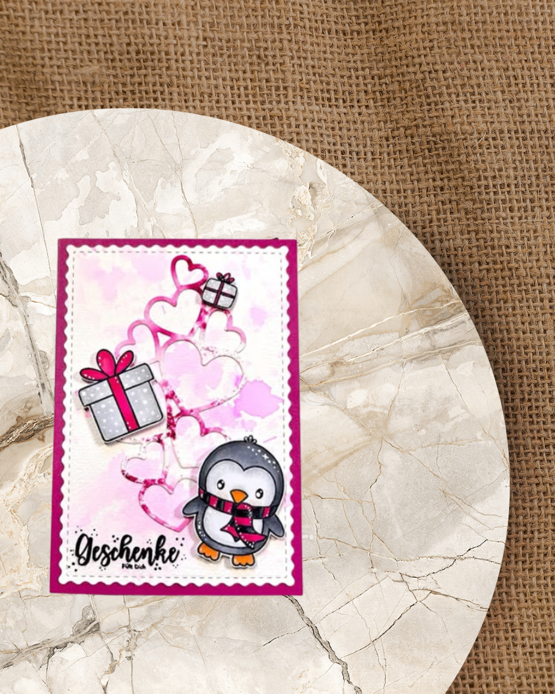 Geschenkkarte mit pinker Mattung und einem Pinguin mit Schal. Im Hintergrund viel rosa Herzen. Dazu ein großes raues Geschenk und ein kleines. Als Spruch Geschenke für dich. 