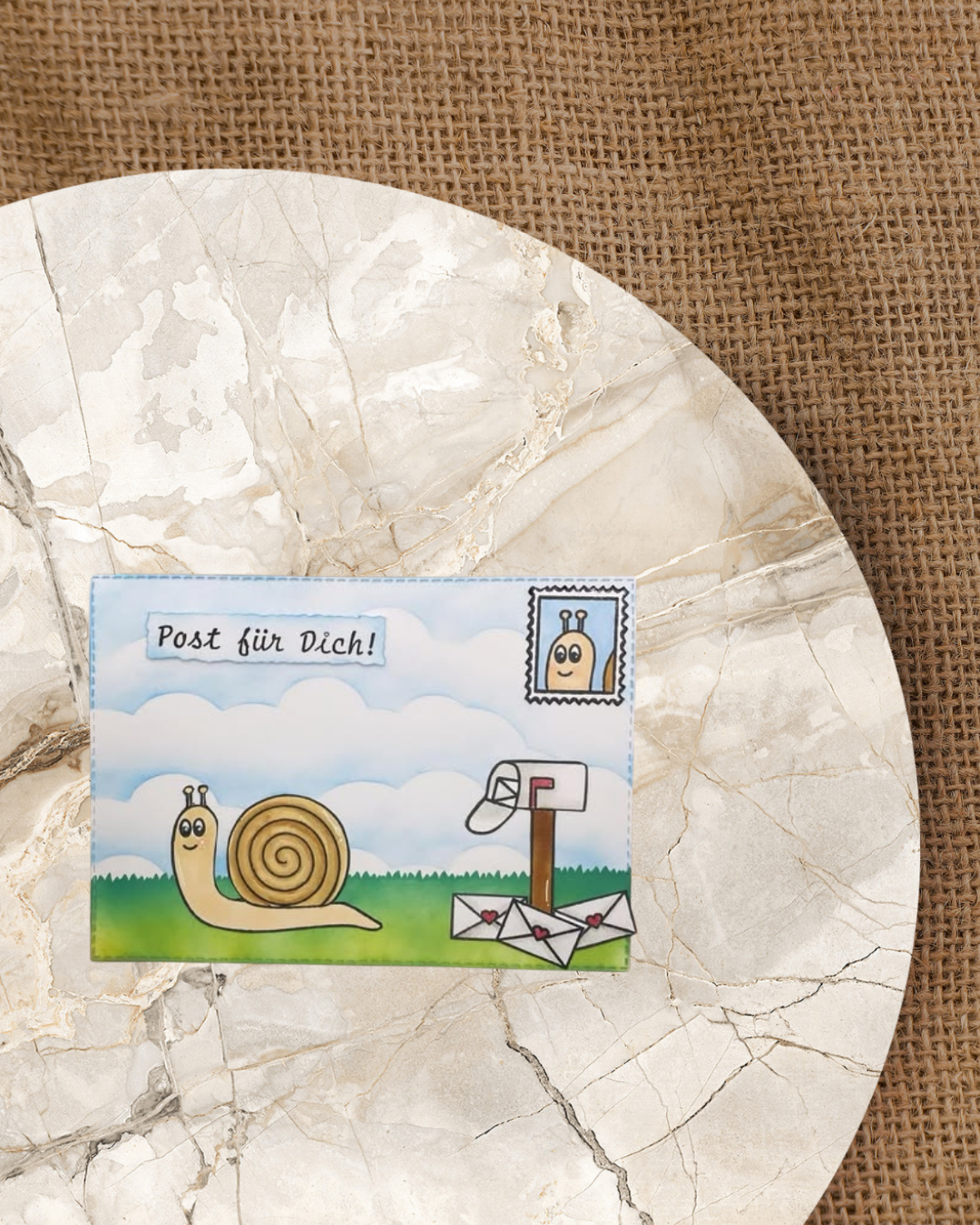 Schnecke auf dem Rasen die gerade von einem Briefkasten mit Briefen auf dem Boden wegkriecht. In der rechten Ecke oben auf der Karte eine Briefmarke mit einem Schneckenkopf. Spruch Post für dich  