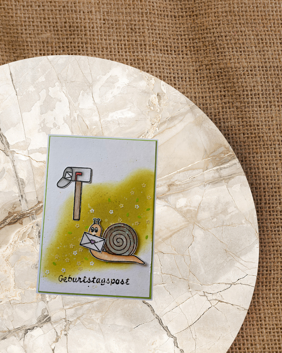 Karte mit einer Schnecke mit einem Briefumschlag im Mund. im Hintergrund ein offener Briefkasten. Spruch Geburtstagspost