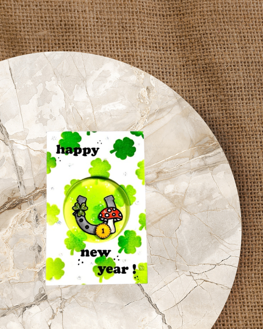 Karte mit einem Hufeisen einem Cent Stück und einem Glückspilz. im Hintergrund Kleeblätter in den Farben  Hell und Dunkelgrün. Als Spruch Happy new year