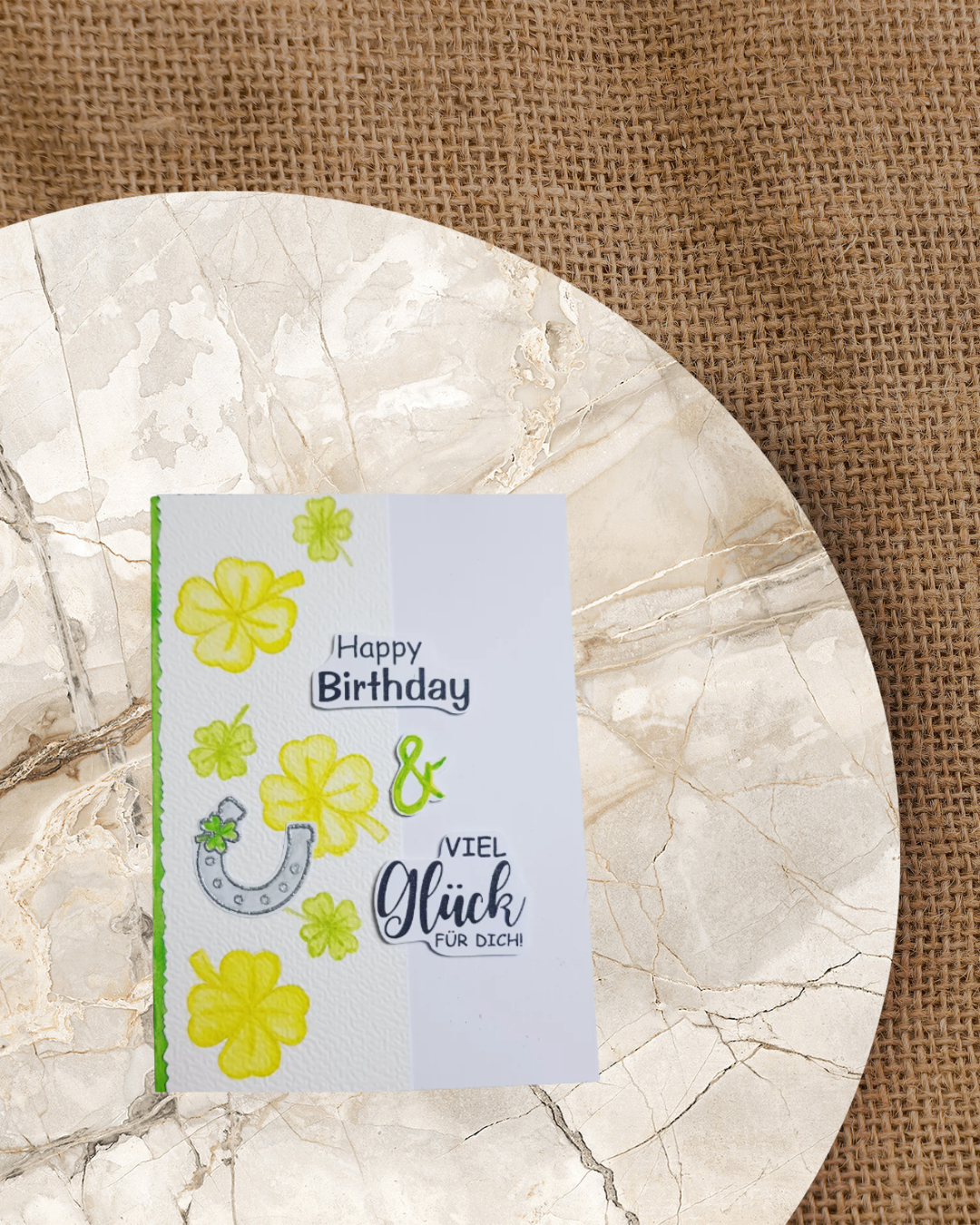 Karte mit grün/gelben Kleeblättern und einem Hufeisen auf der linken Kartenseite angeordnet. Dazu den Spruch Happy Birthday und viel Glück für dich. 